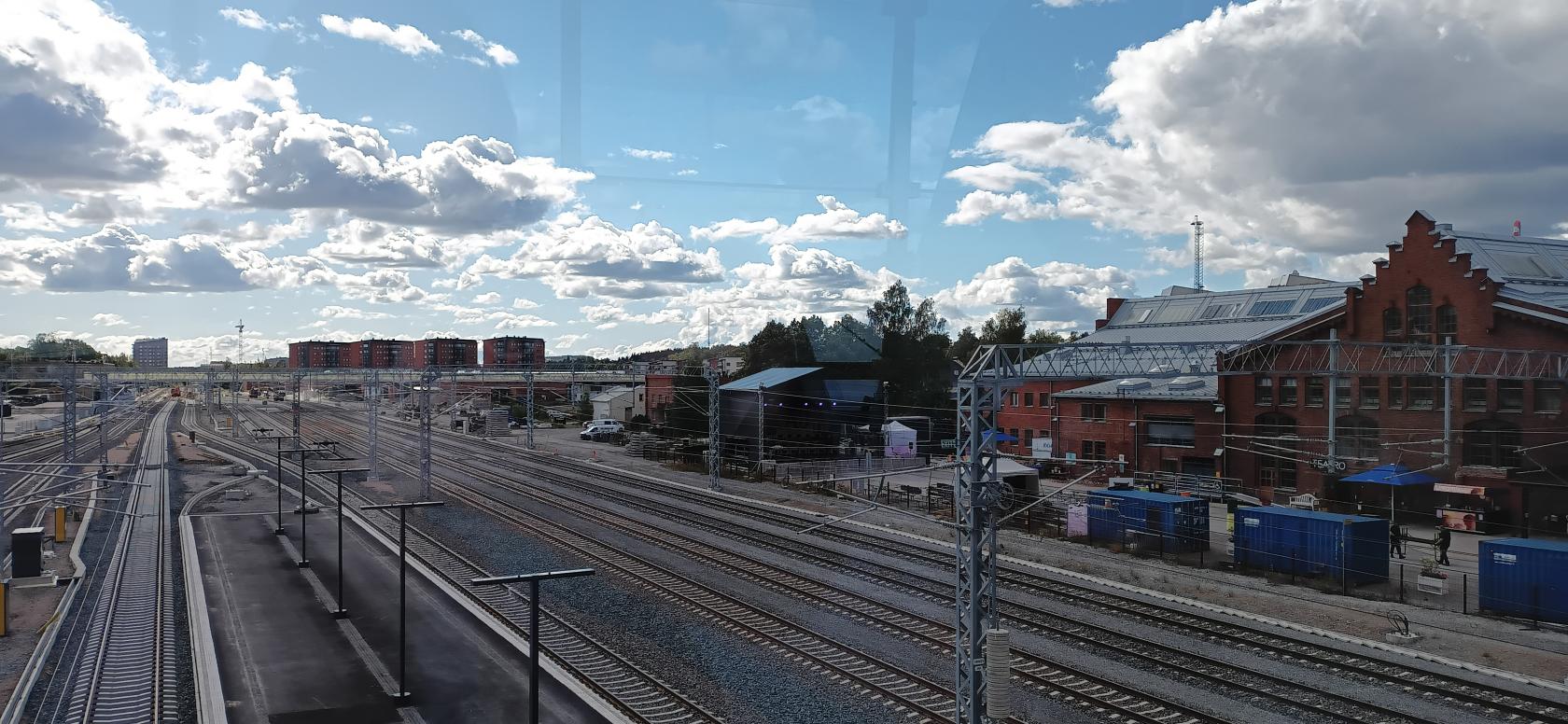 A photograph of a Turku train station. The photo is taken from an elevated position, showing the various lines going through the station, as well as work vehicles on those lines, and an outdoor concert style stage in the back right
